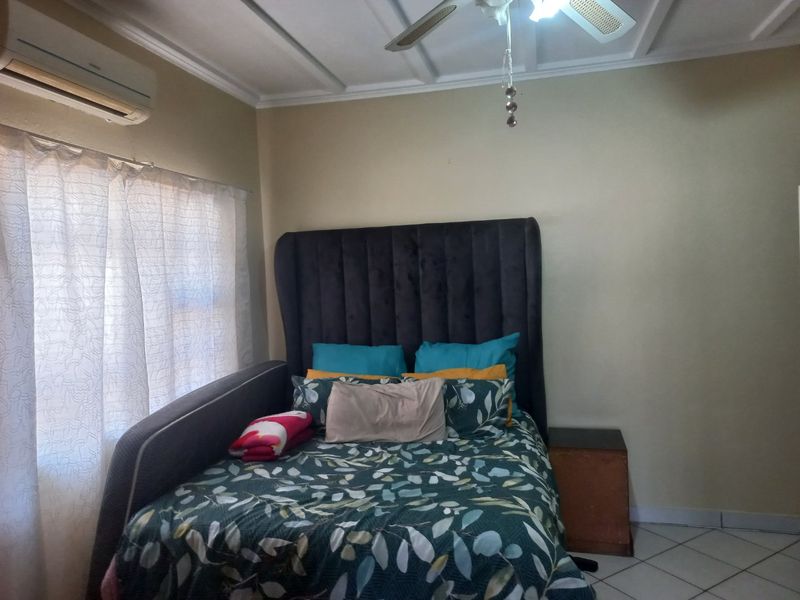 A bedroom featuring tiled flooring, a ceiling fan, and a wall-mounted split-system air conditioning unit.