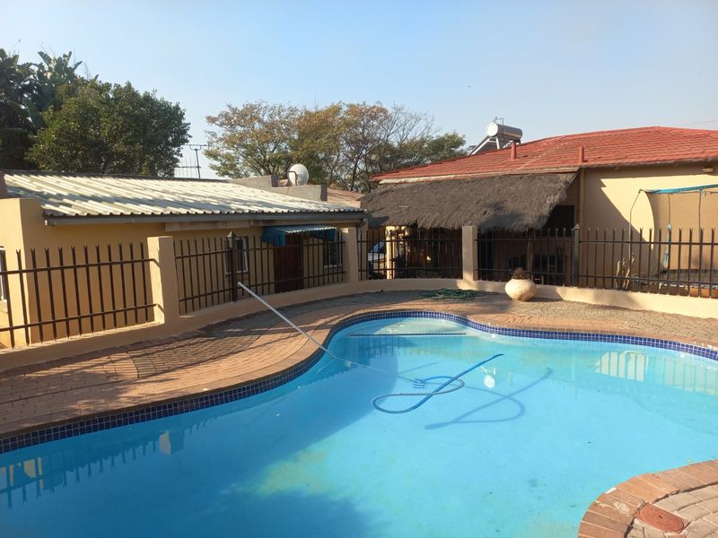 Outdoor pool area featuring a paved surround, metal perimeter fencing, and a secondary structure with a thatched roof and solar water heating system.