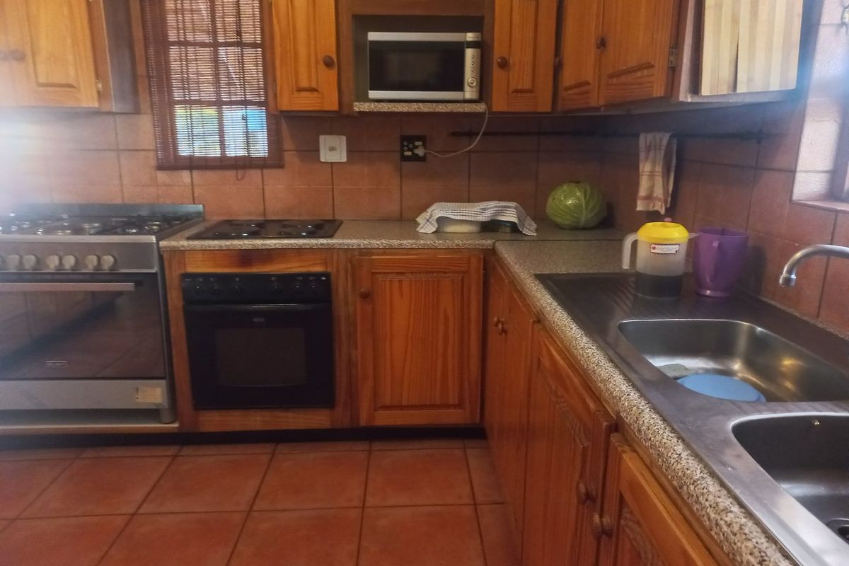 A functional kitchen featuring wooden cabinetry, granite-look countertops, a double sink, and a combination of gas and electric cooking appliances.