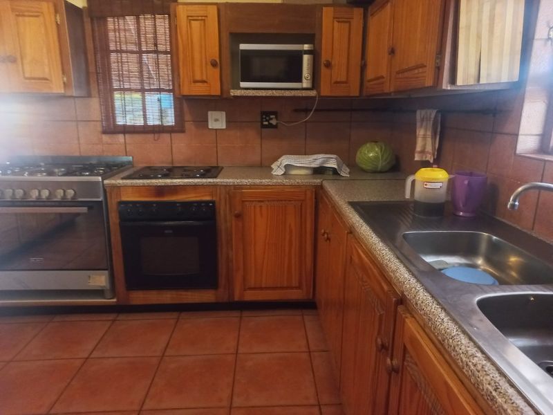 A functional kitchen featuring wooden cabinetry, granite-look countertops, a double sink, and a combination of gas and electric cooking appliances.
