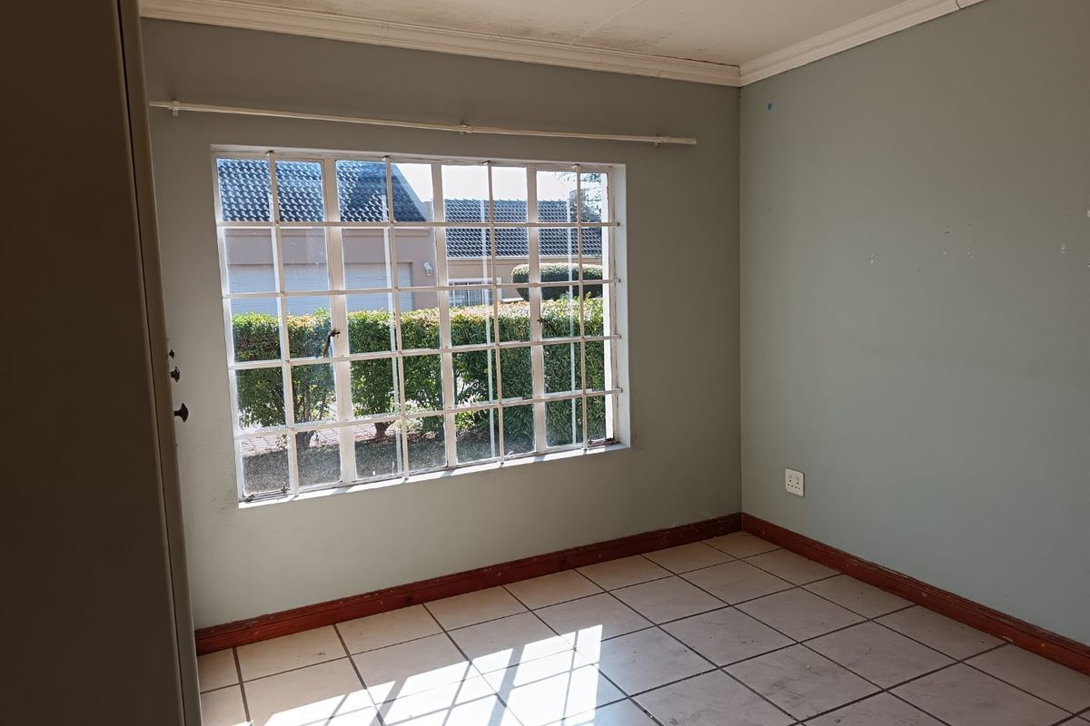 An empty bedroom featuring tiled flooring, security bars on the window, and neutral wall paint, ready for renovation or staging.