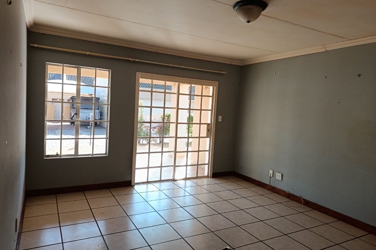 An empty living room featuring tiled flooring, a sliding glass door leading to the exterior, and security bars on the windows.