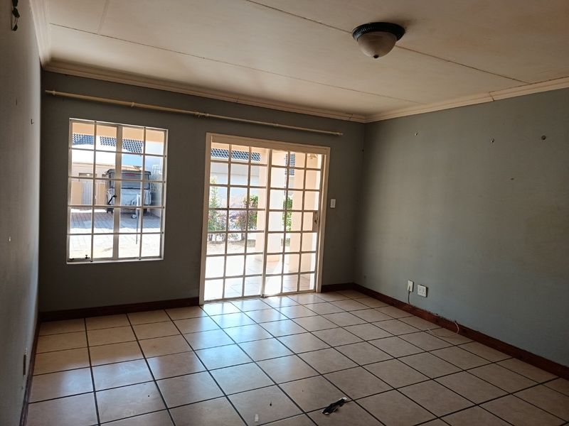 An empty living room featuring tiled flooring, a sliding glass door leading to the exterior, and security bars on the windows.