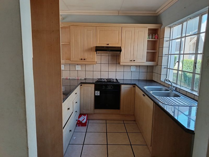 A functional kitchen featuring light wood cabinetry, granite countertops, a built-in oven with hob, and a double basin sink with natural light.