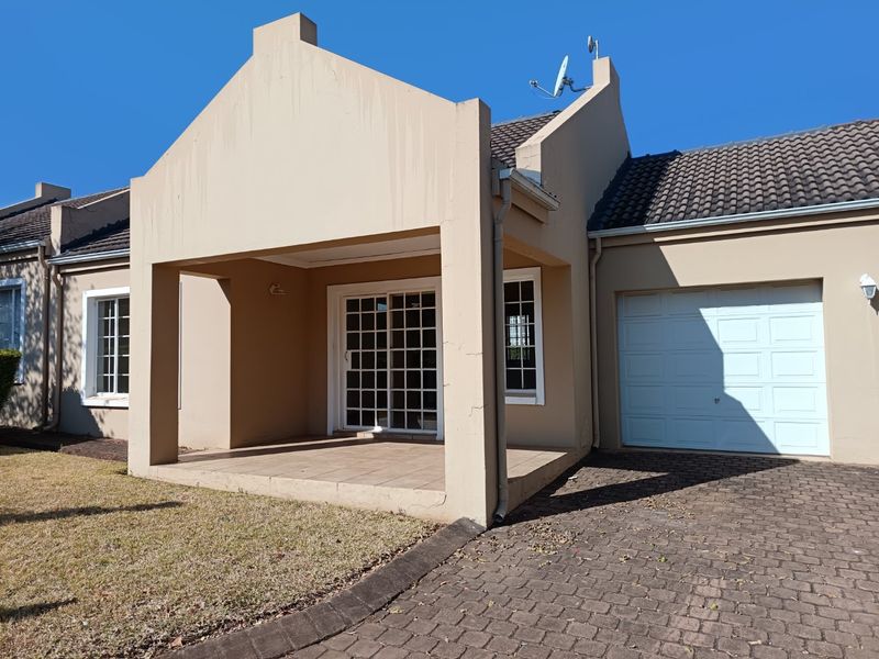 Front elevation of a townhouse featuring a covered patio entrance, paved driveway, and single garage door.