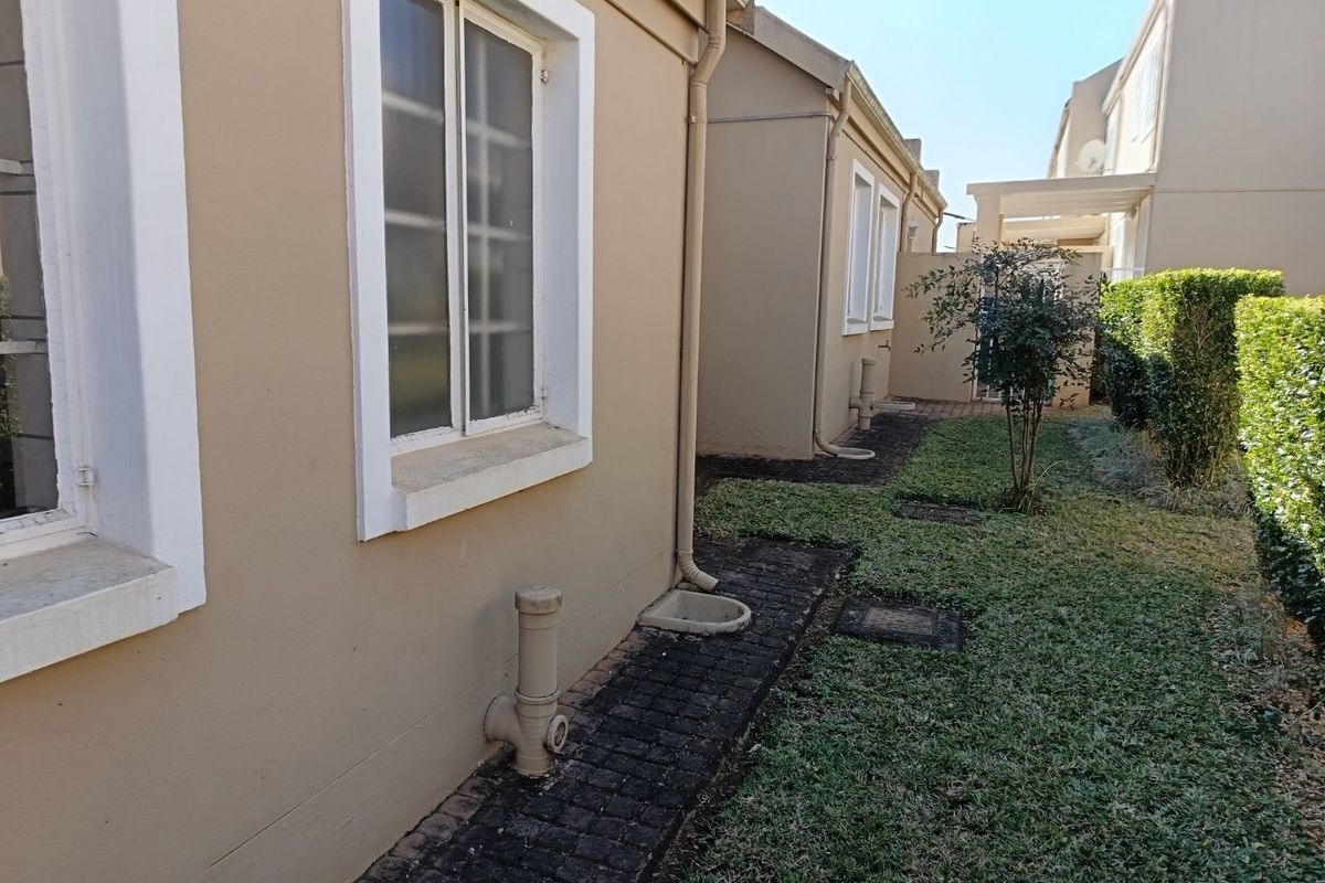 A view of the rear exterior of the townhouse, featuring a paved walkway, lawn area, and established hedging along the boundary.