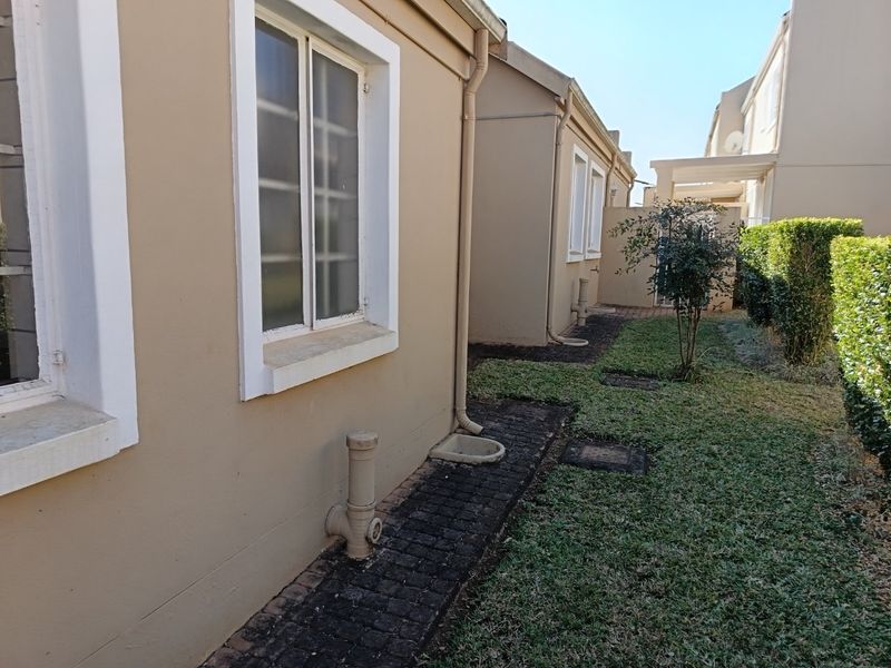 A view of the rear exterior of the townhouse, featuring a paved walkway, lawn area, and established hedging along the boundary.