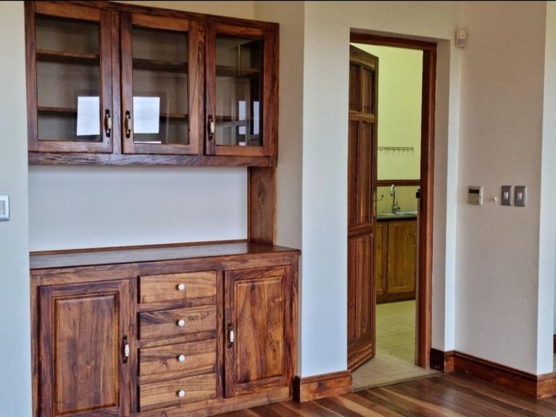 A living area featuring built-in wooden cabinetry and hardwood flooring, with a doorway leading to an adjacent utility or kitchen space.