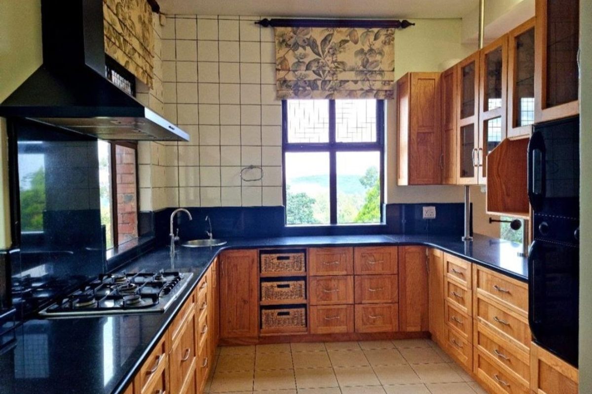 A functional kitchen featuring wooden cabinetry, black granite countertops, a gas hob, and an integrated oven with a view through the window.