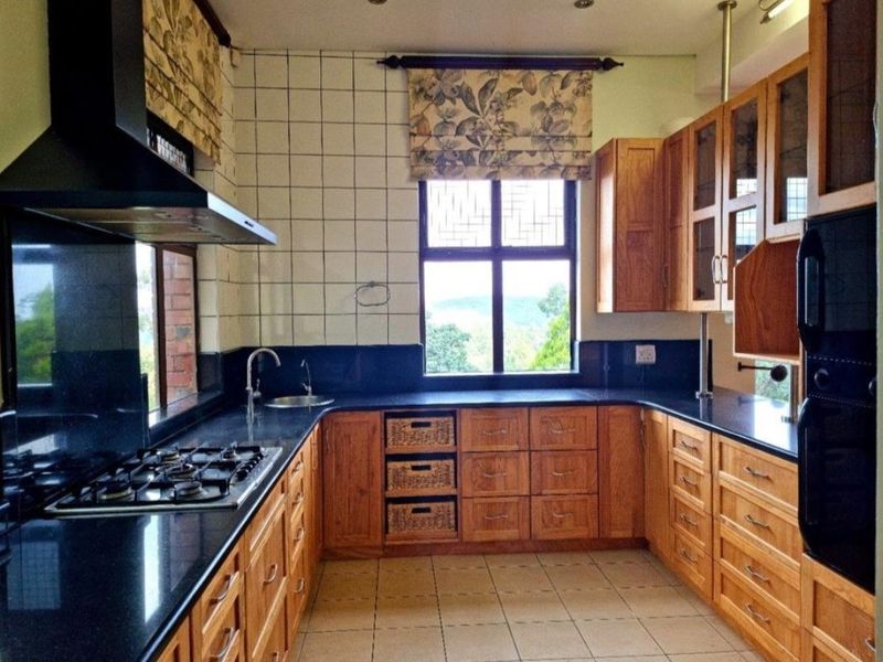 A functional kitchen featuring wooden cabinetry, black granite countertops, a gas hob, and an integrated oven with a view through the window.