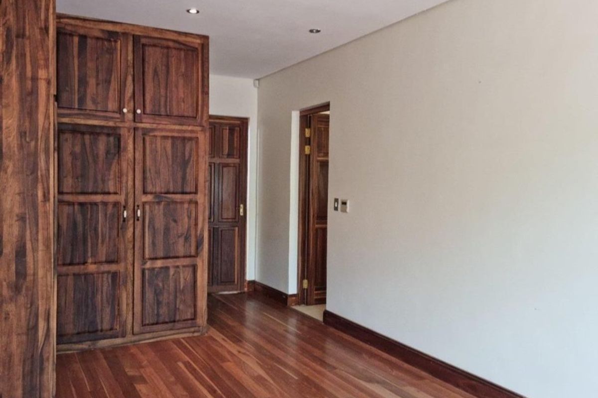 A bright, empty bedroom featuring polished hardwood flooring, recessed ceiling lighting, and a large built-in wooden wardrobe.