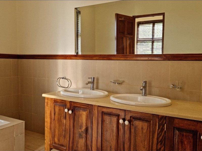A spacious bathroom featuring a double vanity with wooden cabinetry, chrome fixtures, a large wall mirror, and neutral wall tiling.