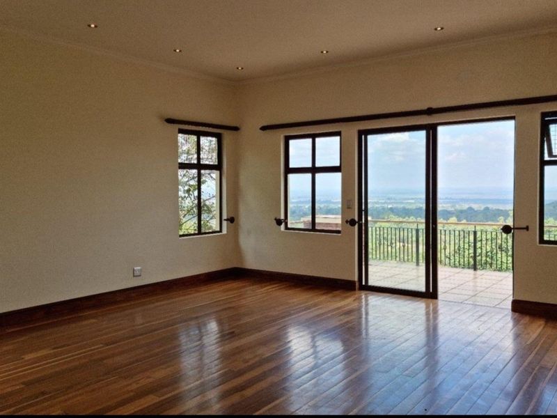 Spacious living room featuring polished hardwood flooring, recessed lighting, and large sliding glass doors opening onto a balcony with scenic views.