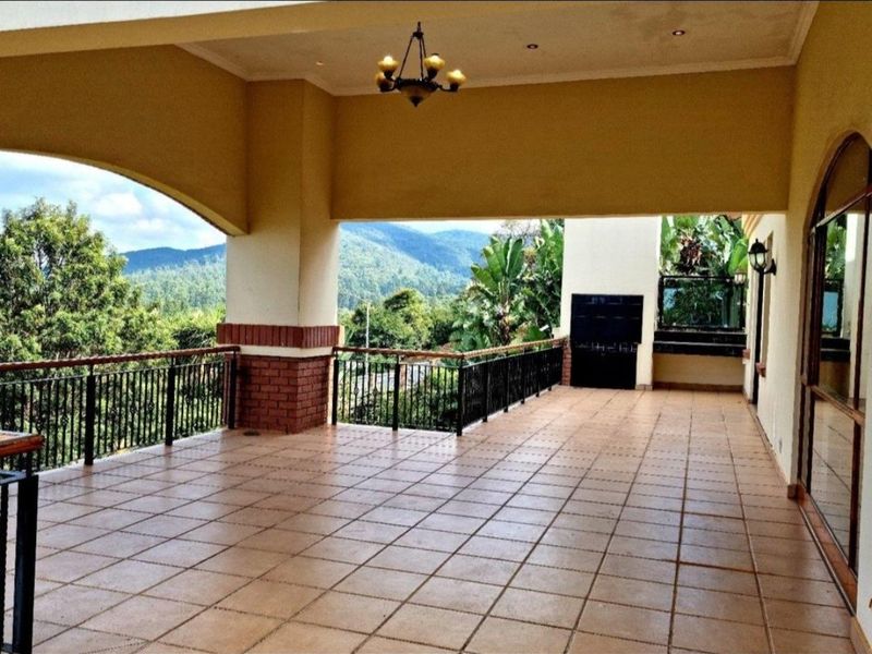 Spacious covered patio featuring tiled flooring, a built-in braai, and wrought iron railings, offering expansive mountain views.