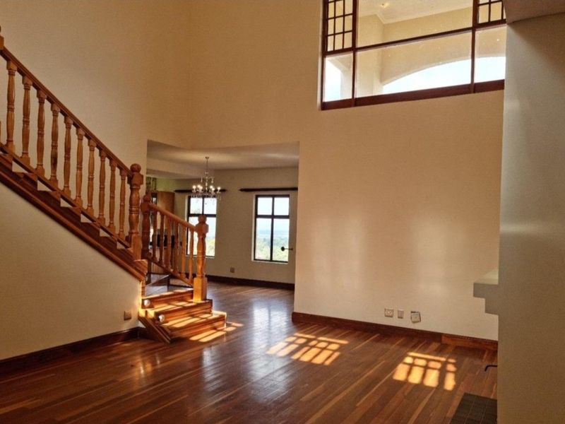 Spacious double-volume living area featuring polished hardwood flooring, a classic wooden staircase with balustrade, and an internal feature window.