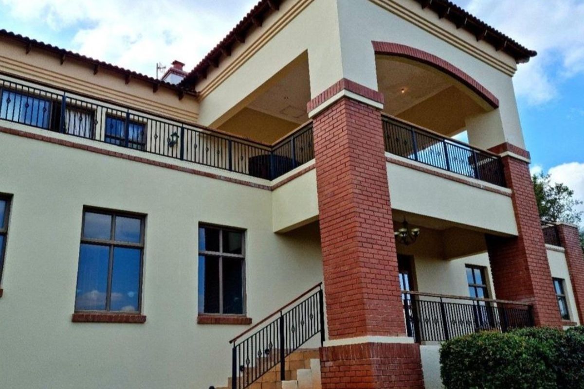 A multi-story residential exterior featuring brick pillar accents, wrought iron balcony railings, and a covered upper-level terrace.