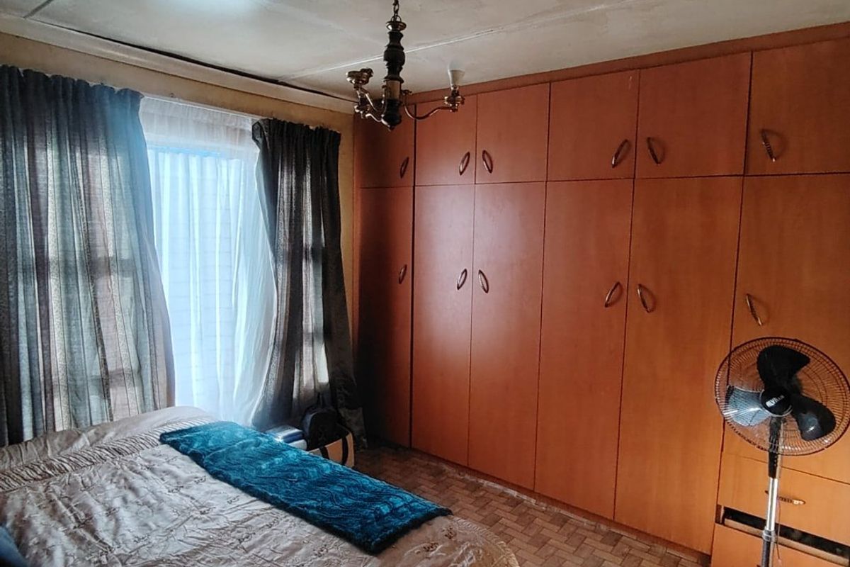 A bedroom featuring extensive built-in wooden cupboards and tiled flooring, requiring some ceiling maintenance and cosmetic updates to modernize the space.