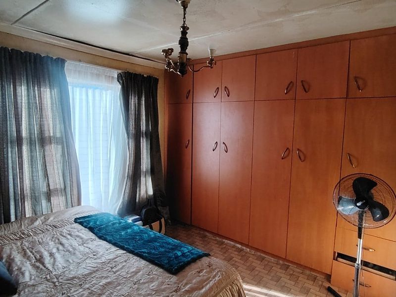 A bedroom featuring extensive built-in wooden cupboards and tiled flooring, requiring some ceiling maintenance and cosmetic updates to modernize the space.