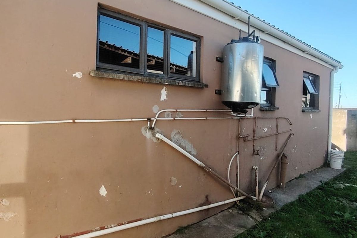 Rear exterior view of the property showing exposed plumbing, an external geyser, and weathered wall finishes requiring maintenance.
