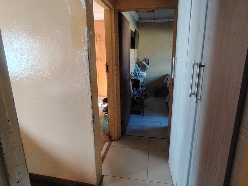 A narrow hallway featuring tiled flooring and built-in cupboards, showing significant signs of wear and damage to the wall finishes.
