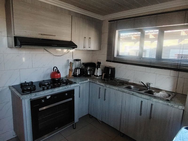 A functional kitchen featuring light wood-grain cabinetry, a gas hob with extractor fan, built-in oven, and a double sink with tiled backsplash.