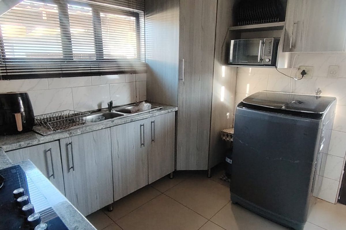 A functional kitchen featuring light wood-grain cabinetry, granite countertops, a built-in gas hob, and integrated microwave space with tiled flooring.