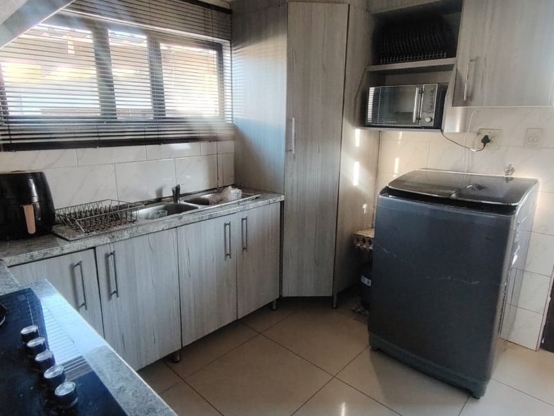 A functional kitchen featuring light wood-grain cabinetry, granite countertops, a built-in gas hob, and integrated microwave space with tiled flooring.