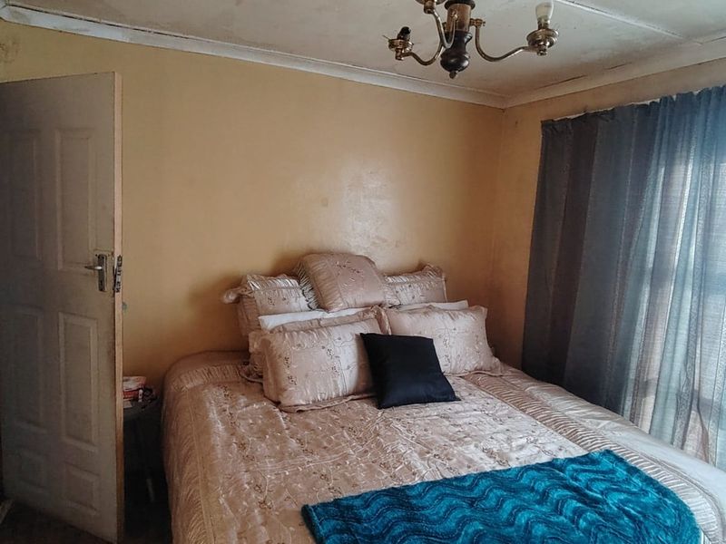 A bedroom featuring a ceiling chandelier and panel door, currently showing significant signs of wear including ceiling water damage and peeling paint.