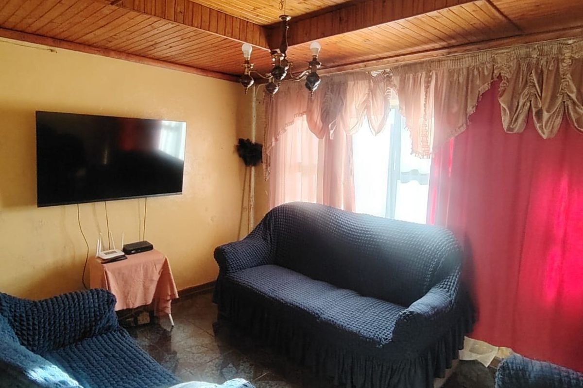 A living room featuring a timber-clad ceiling, tiled flooring, and a central chandelier, offering a dated aesthetic ready for modernization.