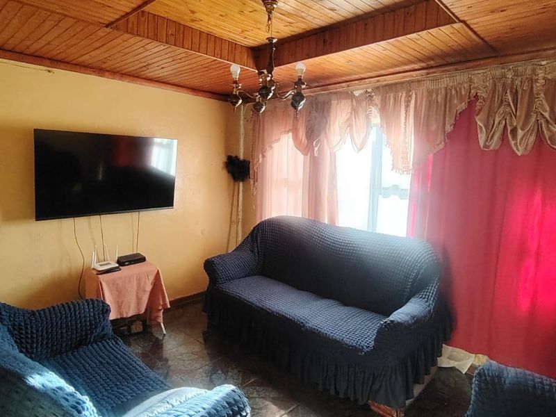A living room featuring a timber-clad ceiling, tiled flooring, and a central chandelier, offering a dated aesthetic ready for modernization.