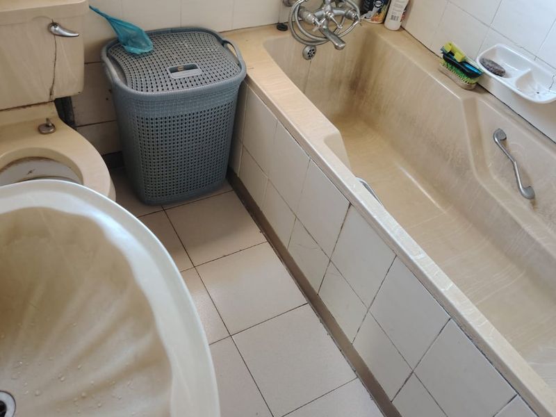 A dated bathroom featuring a bathtub, toilet, and washbasin with visible wear and staining on the sanitary ware and tiling.