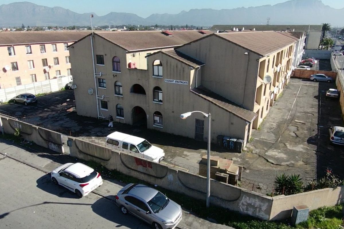 Aerial view of the Radiant Apartments complex, featuring a multi-story residential building with an adjacent paved parking area and perimeter boundary wall.