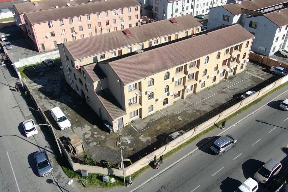Aerial view of a multi-story apartment complex featuring a tiled roof, perimeter wall, and paved parking area.