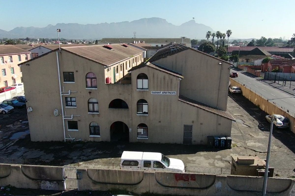 Aerial view of the Radiant Apartments complex, featuring a multi-story residential building with a tiled roof, perimeter wall, and paved parking area.