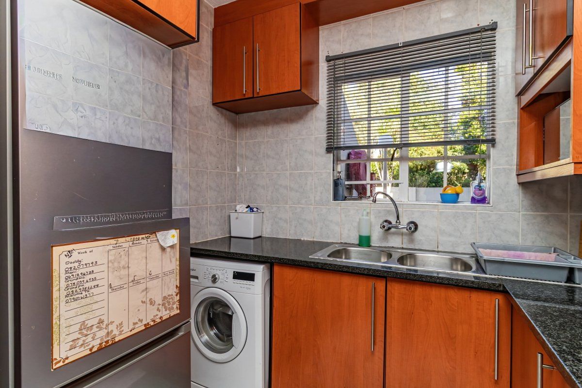 A functional kitchen featuring laminate cabinetry, granite countertops, a double stainless steel sink, and tiled splashbacks with a window view.