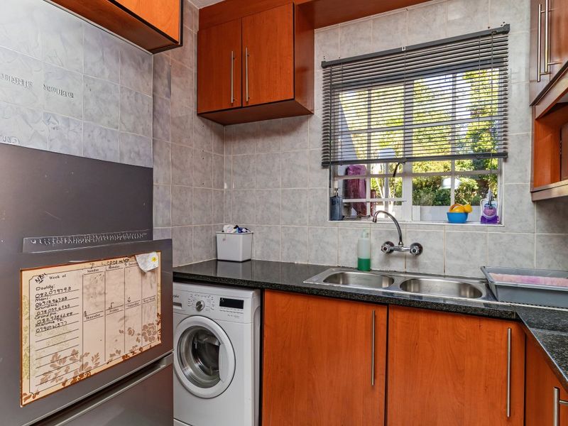 A functional kitchen featuring laminate cabinetry, granite countertops, a double stainless steel sink, and tiled splashbacks with a window view.