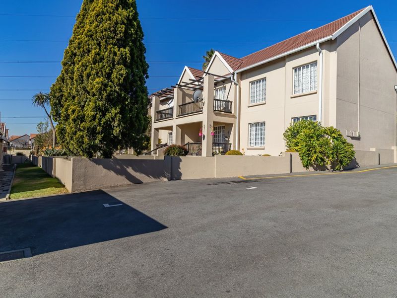 Exterior view of a multi-story apartment complex featuring balconies, tiled roofing, and a paved driveway area.