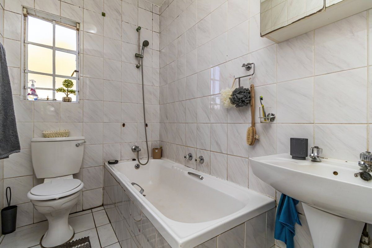A functional bathroom featuring a bathtub with shower attachment, pedestal basin, and toilet, finished with classic wall and floor tiling.