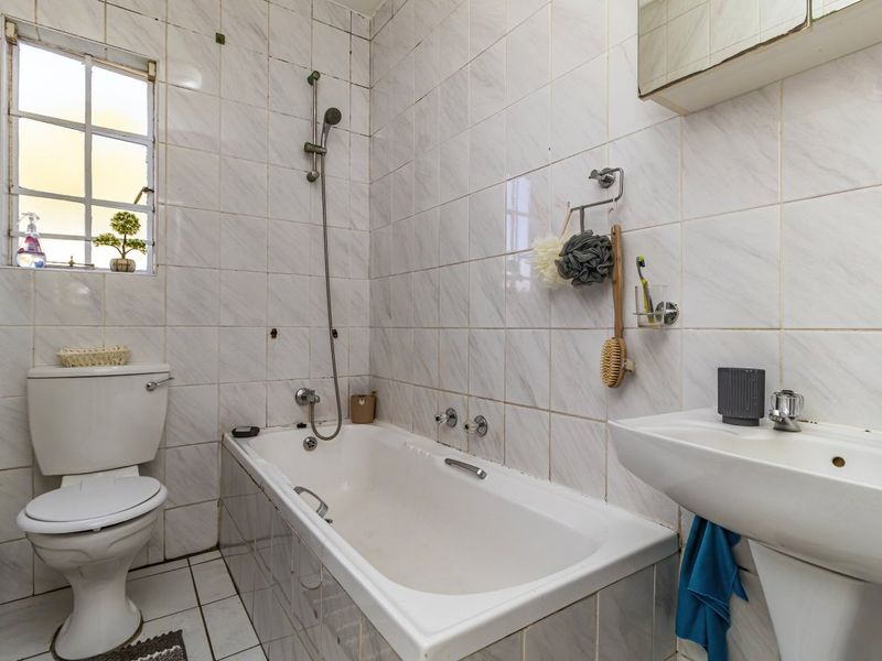 A functional bathroom featuring a bathtub with shower attachment, pedestal basin, and toilet, finished with classic wall and floor tiling.