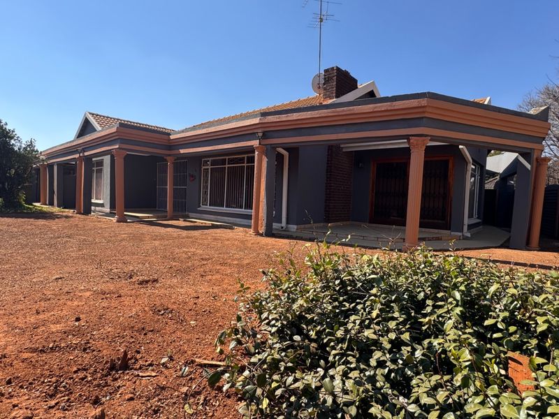Rear view of the house featuring a covered patio, brick chimney, and decorative columns, set against an unlandscaped yard.