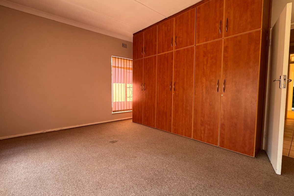 A spacious bedroom featuring extensive built-in wooden cupboards, neutral wall finishes, and carpeted flooring, offering a blank canvas for personalization.