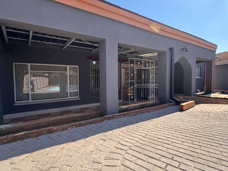 Rear exterior view of the house featuring a covered patio area, security gates, and paved outdoor space.