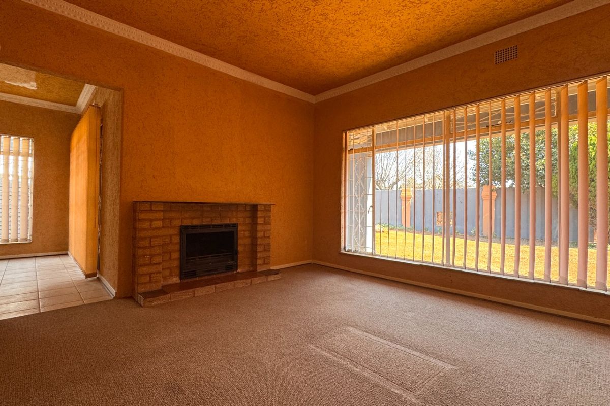 Spacious living room featuring a brick fireplace, large windows with vertical blinds, and textured wall finishes, offering a blank canvas for renovation.