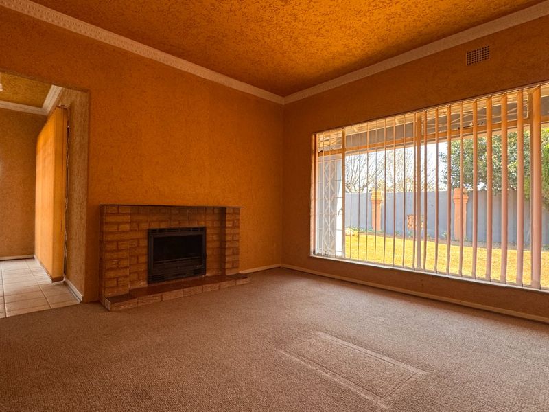 Spacious living room featuring a brick fireplace, large windows with vertical blinds, and textured wall finishes, offering a blank canvas for renovation.
