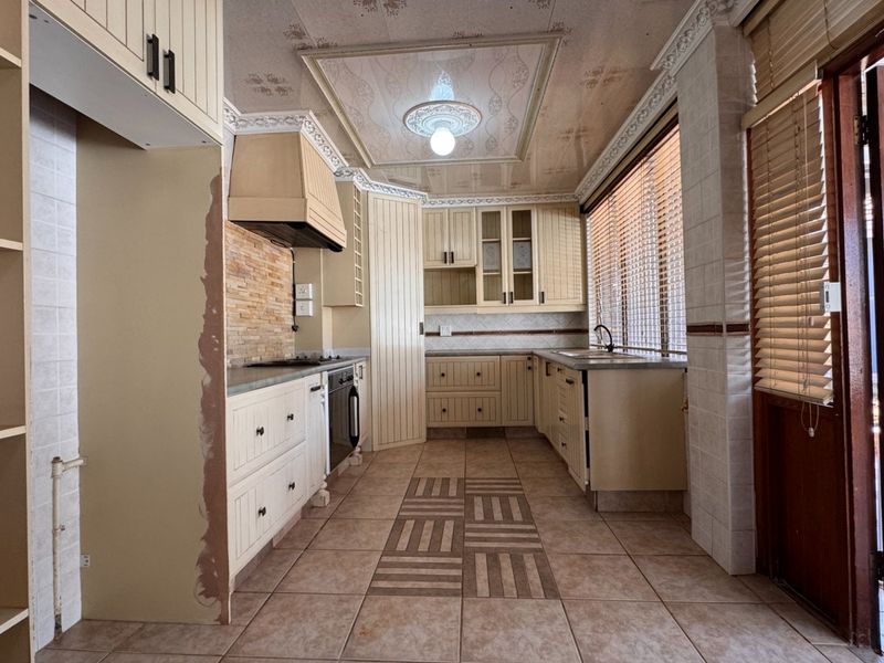 A dated kitchen featuring built-in cabinetry, a hob, oven, and extractor fan, with tiled flooring and direct access to an outdoor patio area.
