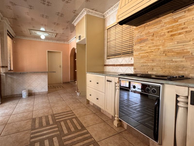 A spacious kitchen featuring built-in cabinetry, a stone tile backsplash, integrated oven and cooktop, and a breakfast bar, offering significant potential for modern renovation.
