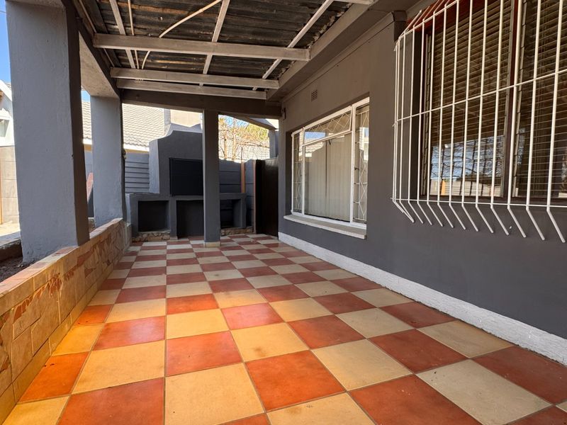 A covered outdoor patio area featuring a built-in braai, tiled flooring, and security bars on the windows.