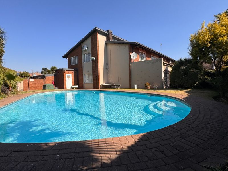 A private swimming pool area featuring brick paving, set against the rear elevation of a townhouse with established garden surroundings.