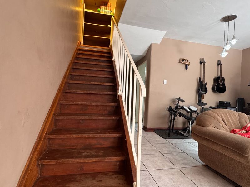 Living area featuring a wooden staircase with metal balustrade, tiled flooring, and pendant lighting, offering a functional layout for the home.