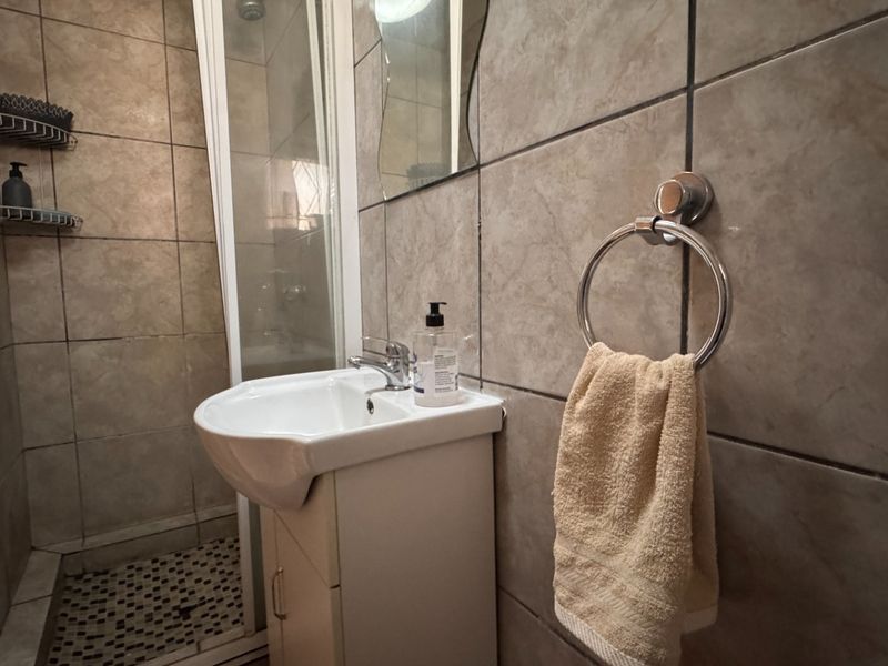 A compact bathroom featuring a shower enclosure, vanity basin with mixer tap, and neutral wall tiling.